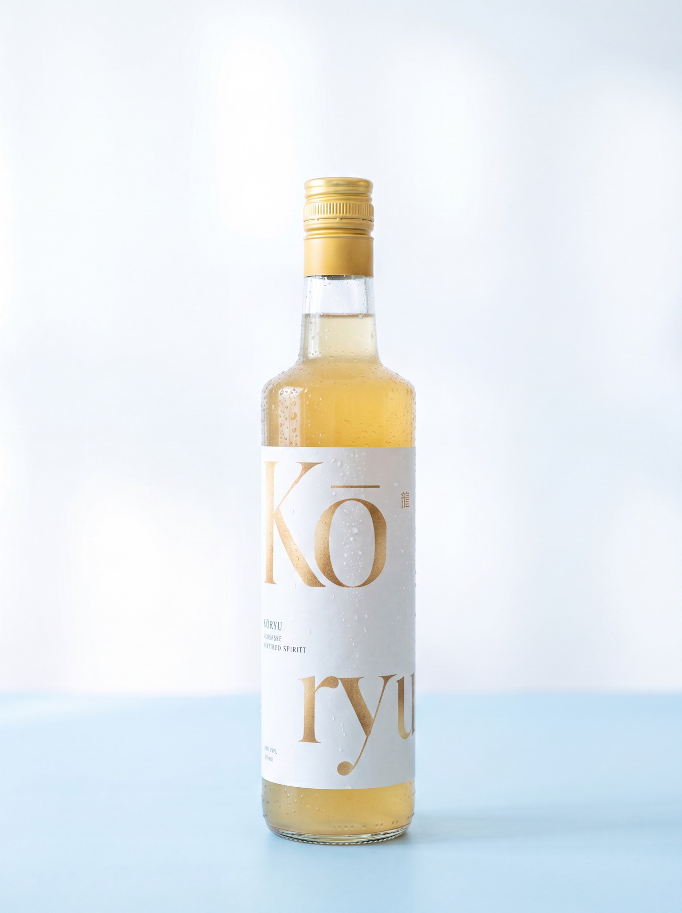 Eine 700-ml-Flasche Kōryu, blassgoldene Spirituose hinter einem cremefarbenen Etikett mit goldener Schrift, vor hellem Studiohintergrund.